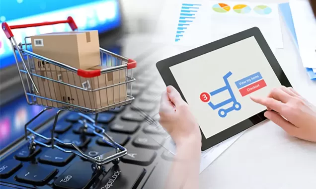 Mini shopping cart with boxes on a computer keyboard next to a person using a tablet for online shopping and checkout